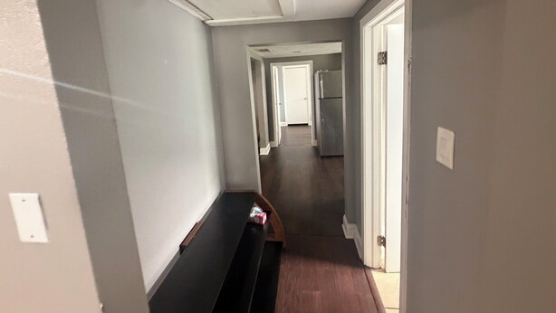 Um corredor com um banco, um frigorífico e uma porta que dá para outro quarto.
