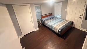 Quarto com uma cama, uma mesinha e uma porta.