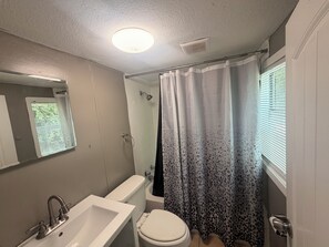 Ein Badezimmer mit weißem Waschbecken, WC und Badewanne. Ein Duschvorhang mit Leopardenmuster.