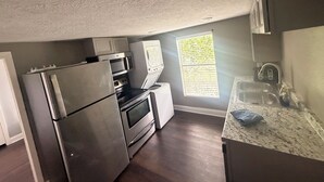 A compact kitchen with a refrigerator, oven, microwave, and a window with blinds.
