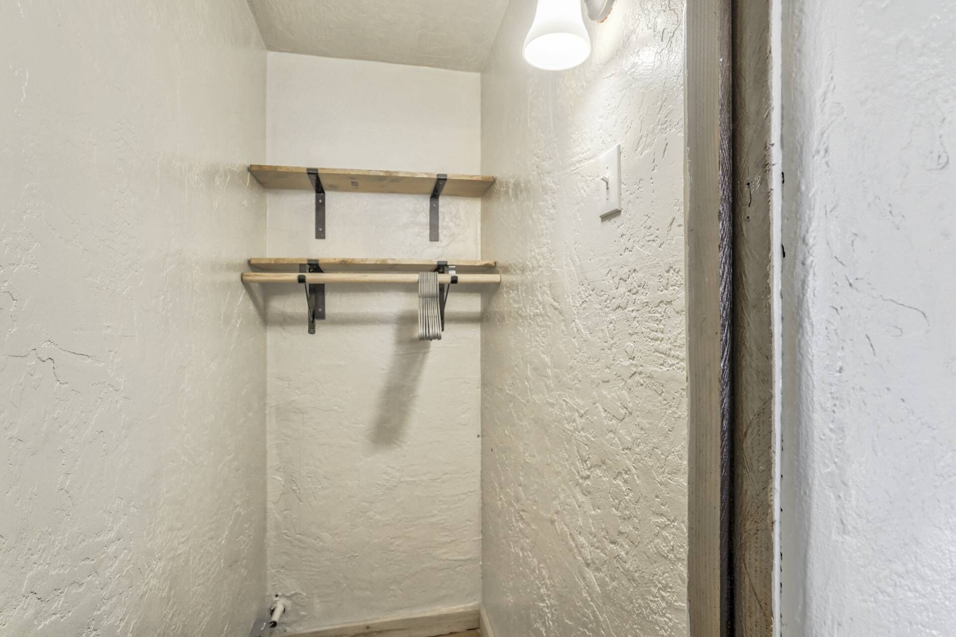A bathroom with white walls, a wooden shelf, and a towel rack.