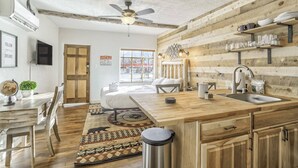 A rustic kitchen with a wooden island, a ceiling fan, and a view of the street outside. - The Birch Room | Pet-Friendly Studio Near Manitou (Colorado Springs)