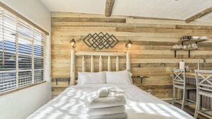 A bedroom with a wooden headboard, a bed with white linens, a decorative wall piece, and a window with blinds. - The Birch Room | Pet-Friendly Studio Near Manitou (Colorado Springs)