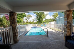 Piscina coberta com parede de pedra e guarda-corpo branco, cercada por área com grade e vista para árvores e um edifício.