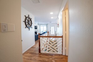A hallway with a wooden floor, a white railing, and a ship's wheel decoration on the wall. - Eikos Beach House - 4 BR / 3 BA - Heated Pool / Spa (Treasure Island)