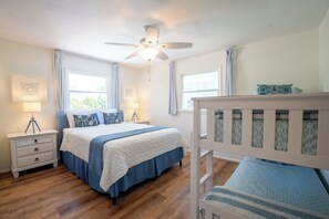 Quarto com cama, mesas de cabeceira, ventilador de teto e janelas.