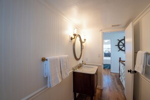 A narrow hallway with a bathroom featuring a sink, mirror, and towel rack. - Eikos Beach House - 4 BR / 3 BA - Heated Pool / Spa (Treasure Island)