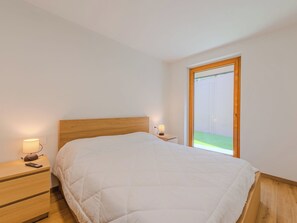 Ein Schlafzimmer mit einem Bett, zwei Nachttischen mit Lampen, einem Holz-Kopfende und einem Fenster mit Blick auf eine grüne Wiese.