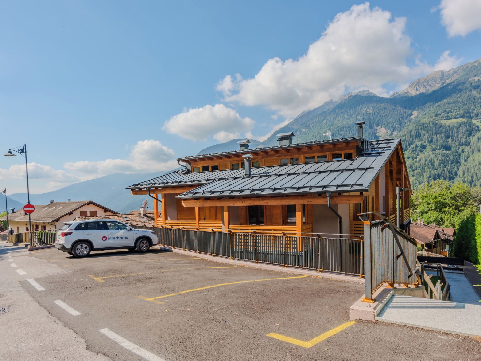 Un bâtiment en bois à deux étages, doté d’un toit en pente, avec une voiture garée devant et des montagnes en arrière-plan.