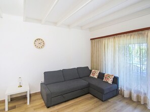 A living room with a grey sectional sofa, a small white side table, and a wall clock. - Hermitage by Interhome (Porto Valtravaglia)
