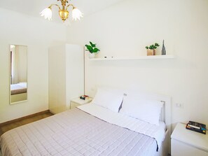 Ein Schlafzimmer mit einem Bett, einem Nachttisch, einem Wandregal mit Pflanzen und einer Pendelleuchte.