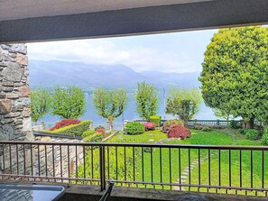Ein Balkon mit Steinmauer, Metallgeländer und Blick auf einen See mit Bergen im Hintergrund.