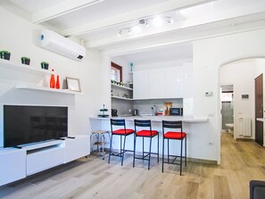 Eine moderne Küche mit weißen Schränken, einem eingebauten Fernseher und einer Bar mit roten Stühlen.