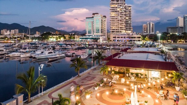 Ein Yachthafen mit Booten, ein Restaurant am Wasser und moderne Gebäude im Hintergrund.