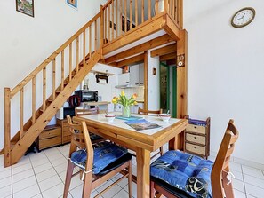 A wooden dining table with chairs, a kitchen area with appliances, and a wooden staircase. - Les Maisons de la Mer by Interhome (Pornic)