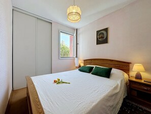 Een hotelkamer met een bed, nachtkastje, lamp, raam en een schilderij aan de muur.