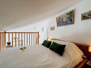 A bedroom with a large bed, two pillows, a wooden headboard, a nightstand, a lamp, and a painting on the wall. - Les Maisons de la Mer by Interhome (Pornic)