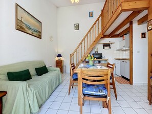 Een gezellige woonkamer met een bank, een eettafel, stoelen, een trap en een keukenhoek.