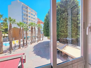 A view of a building with multiple floors and balconies, palm trees, and a paved area with benches. - Apartamento Alba 5 by Interhome (Cartagena)