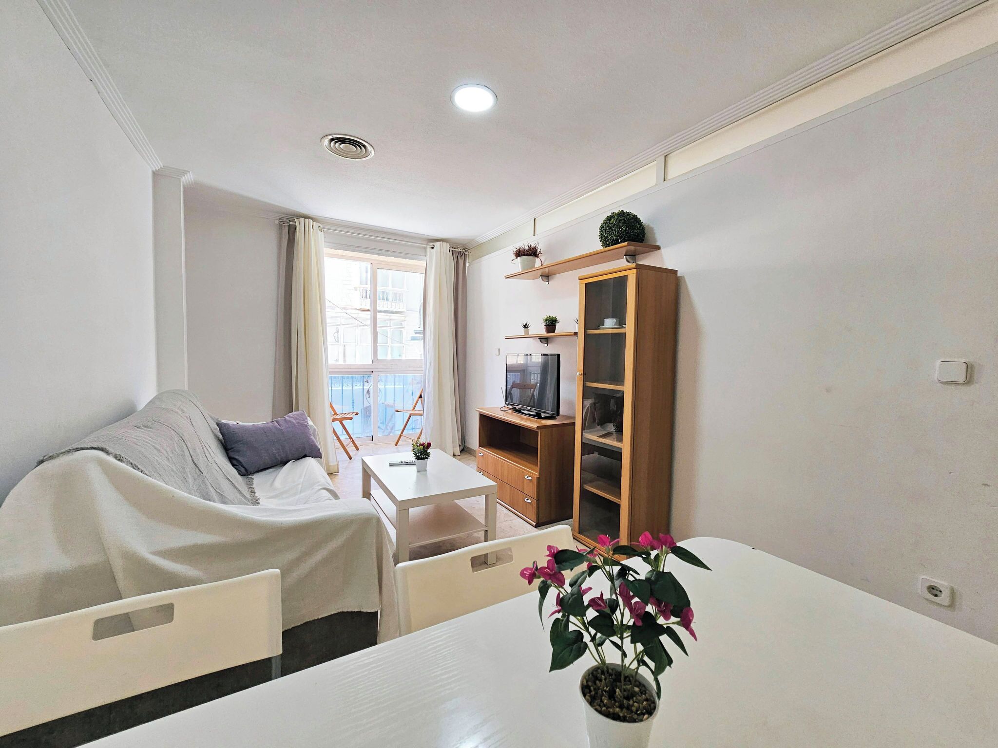 A hotel room with a bed, a small table, a TV, a cabinet, and a window with curtains.
