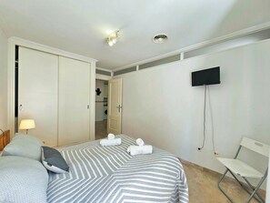 A hotel room with a bed, a TV mounted on the wall, a desk, and a chair. - Apartamento Alba 5 by Interhome (Cartagena)