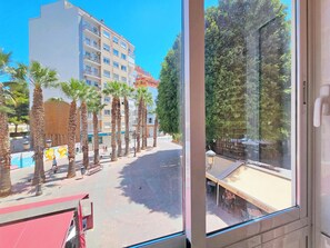 A view of a building with multiple floors and balconies, palm trees, and a paved area with benches. - Apartamento Alba 7 by Interhome (Cartagena)
