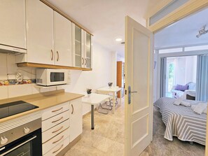 A compact kitchen with a microwave, oven, and cabinets, leading to a dining area with a table and chairs. - Apartamento Alba 7 by Interhome (Cartagena)