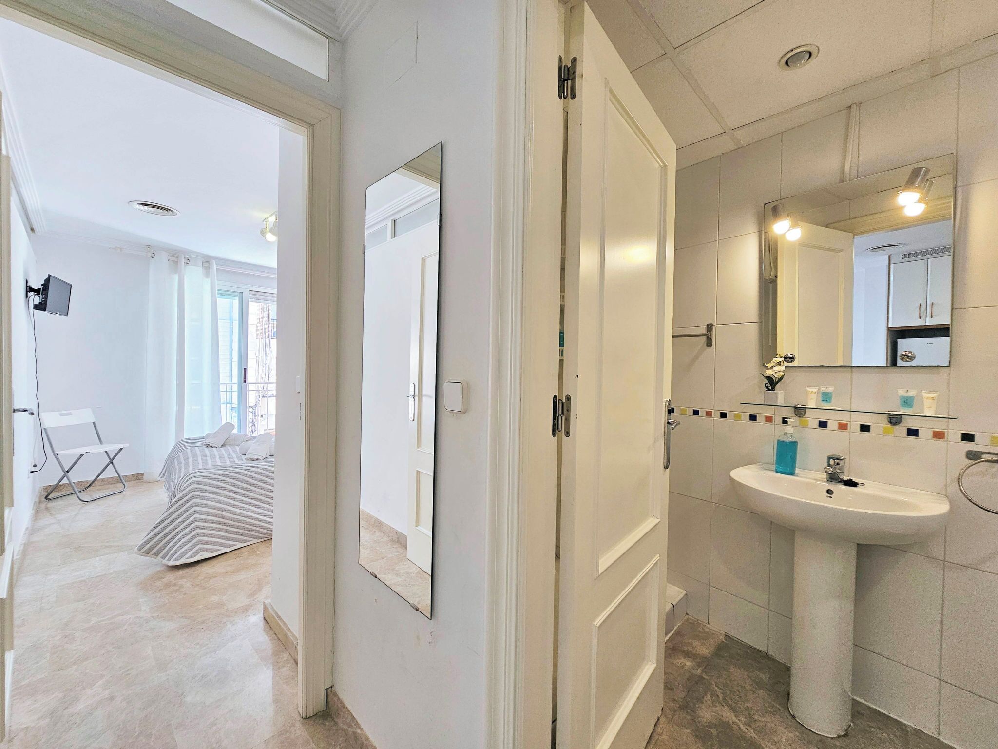A hotel room with a bed, a bathroom with a sink and mirror, and a door leading to another room.