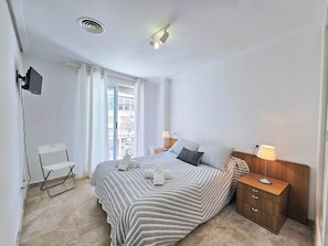 A hotel room with a bed, bedside tables, a desk with a chair, a TV mounted on the wall, and a window with curtains. - Apartamento Alba 8 by Interhome (Cartagena)