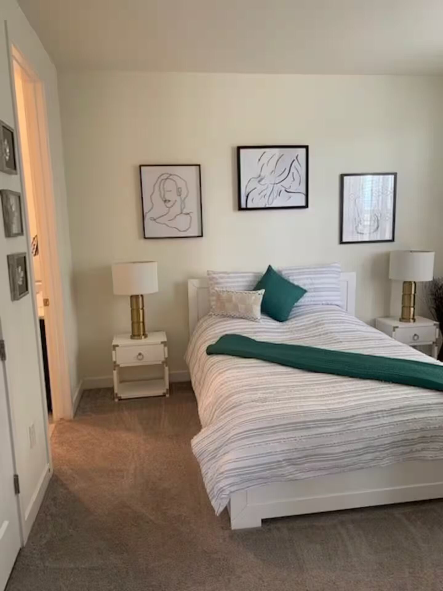 Une chambre à coucher avec un lit, deux tables de chevet, une lampe sur chacune, et trois œuvres d’art encadrées accrochées au mur.