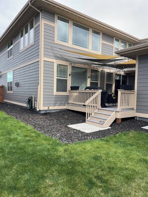 Ein zweistöckiges Haus mit einer Veranda, einem kleinen Sitzbereich im Freien und einem sichtbaren Gartenschlauch.