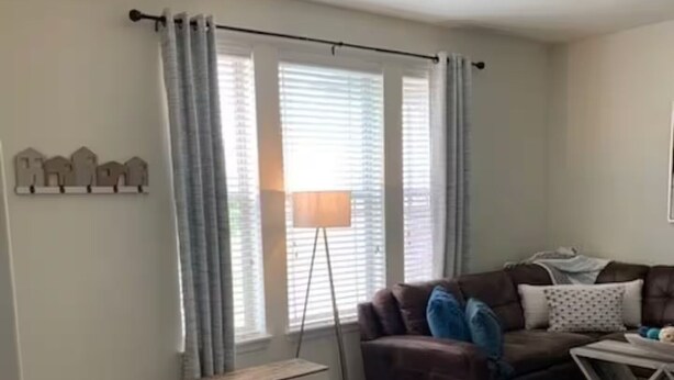 Uma sala de estar com um sofá de couro marrom, um pequeno banco branco, um abajur e uma mesa de jantar com um tapete.