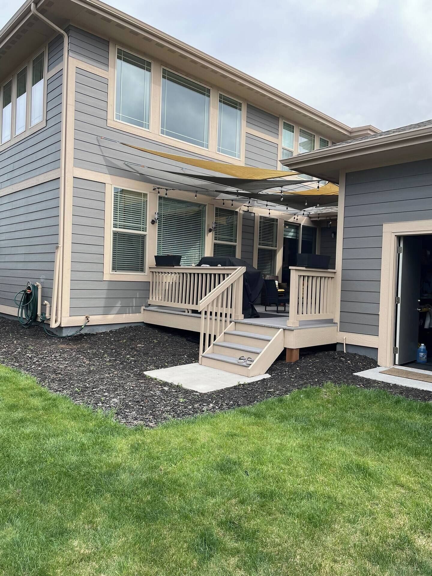 A two-story house with a covered porch, a small outdoor seating area, and a visible garage door.
