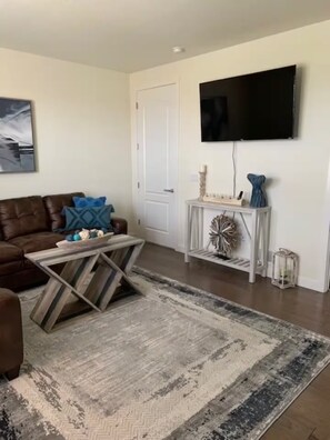A living room with a brown leather sofa, a wooden coffee table, a large rug, a white console table with decorative items, and a flat-screen TV mounted on the wall. - THE PLACE YOU WILL LOVE TO COME BACK AGAIN!!! (Denver)