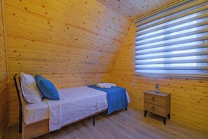 Une chambre individuelle avec un plafond en pente, un lit avec des oreillers, une table de chevet et une fenêtre avec des stores.