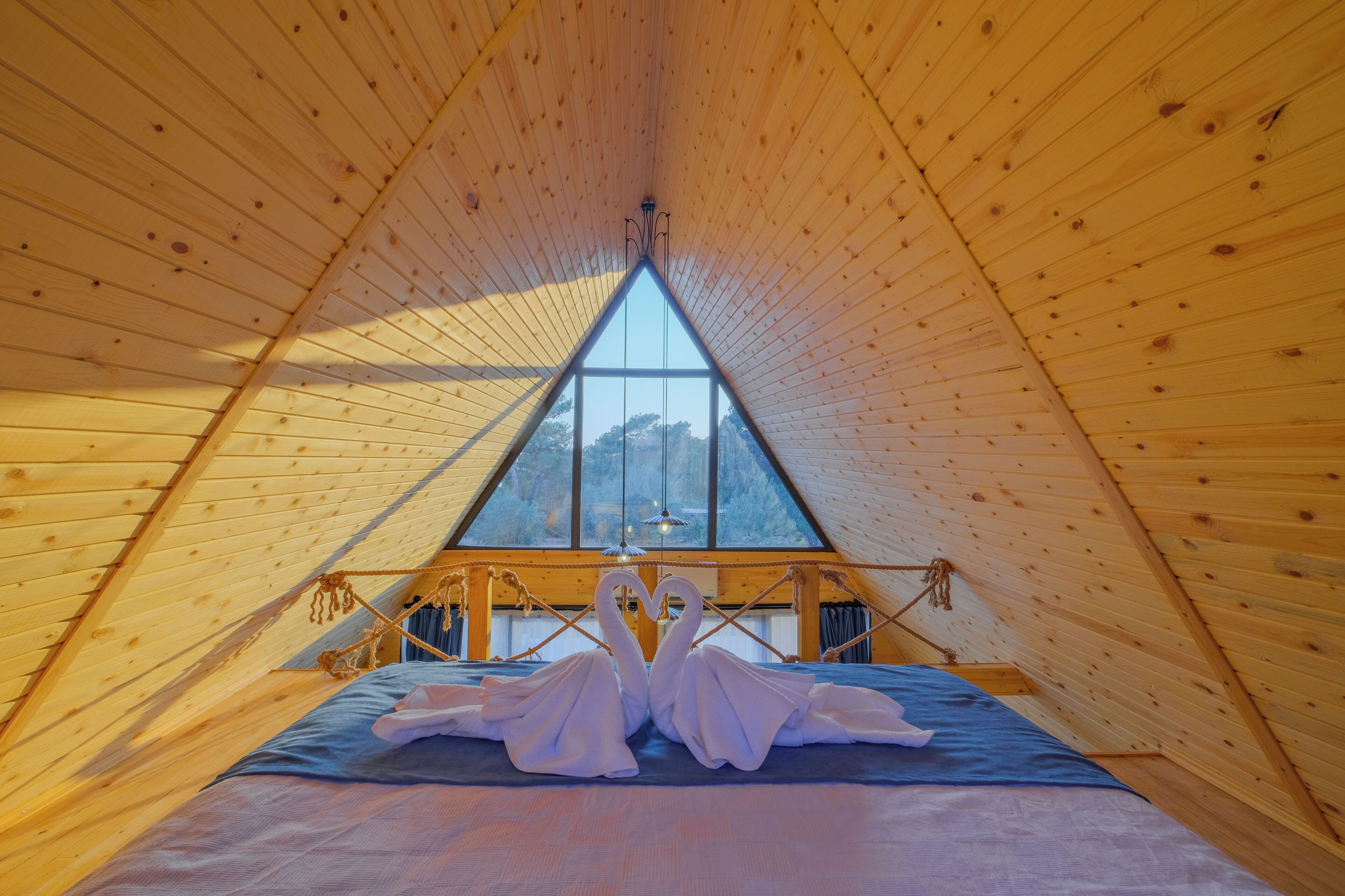 A triangular wooden room with a bed and a large window.