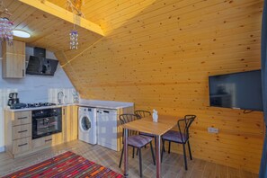 Cocina compacta con lavadora, zona de comedor con sillas y televisor de pantalla plana montado en la pared.