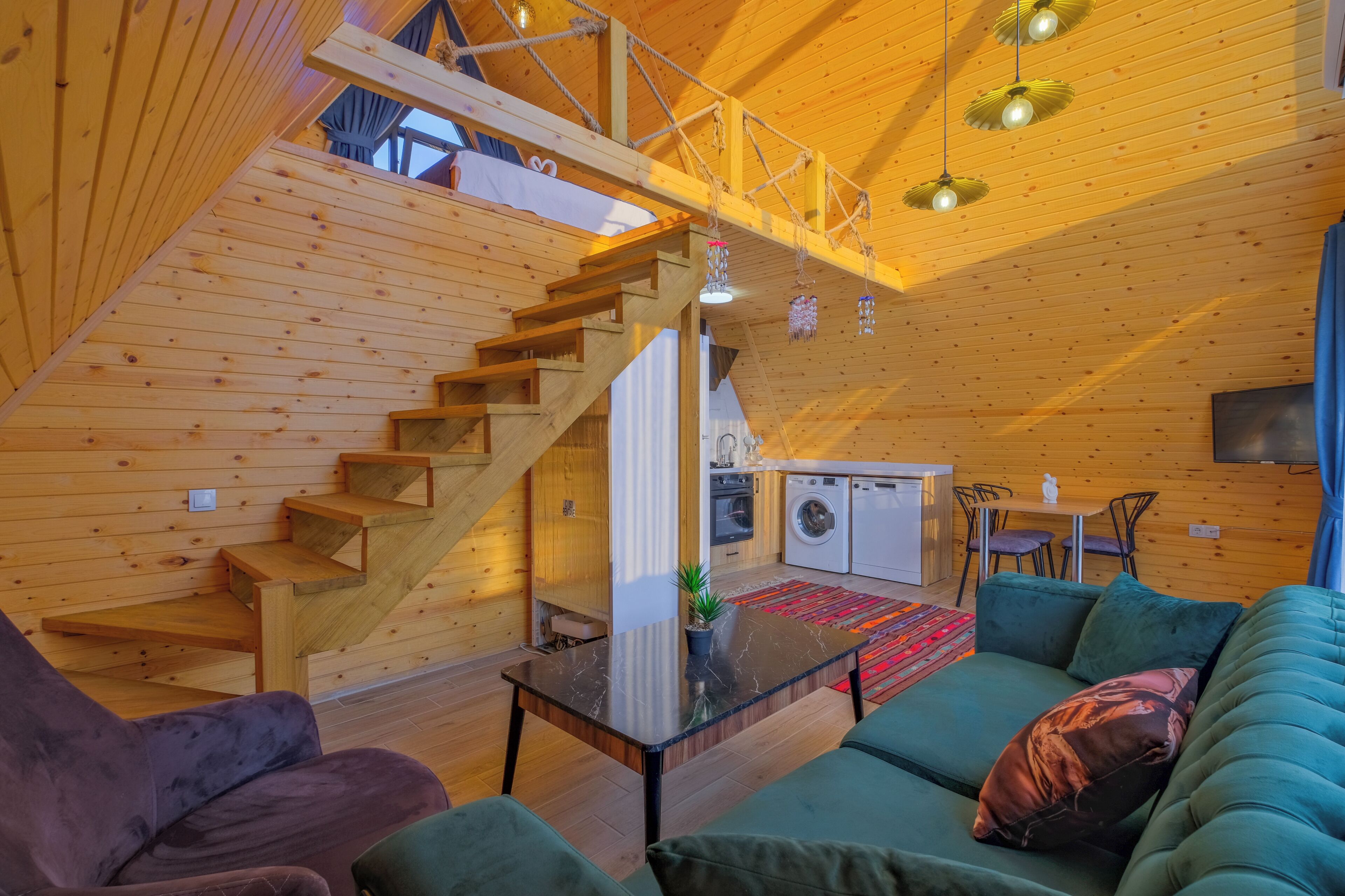 A wooden interior with a staircase, a sofa, a washing machine, and a television.