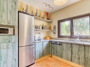 A kitchen with a stainless steel refrigerator, a microwave, a dishwasher, and a window with a view of trees. - Sunrise by Interhome (Vilajuiga)