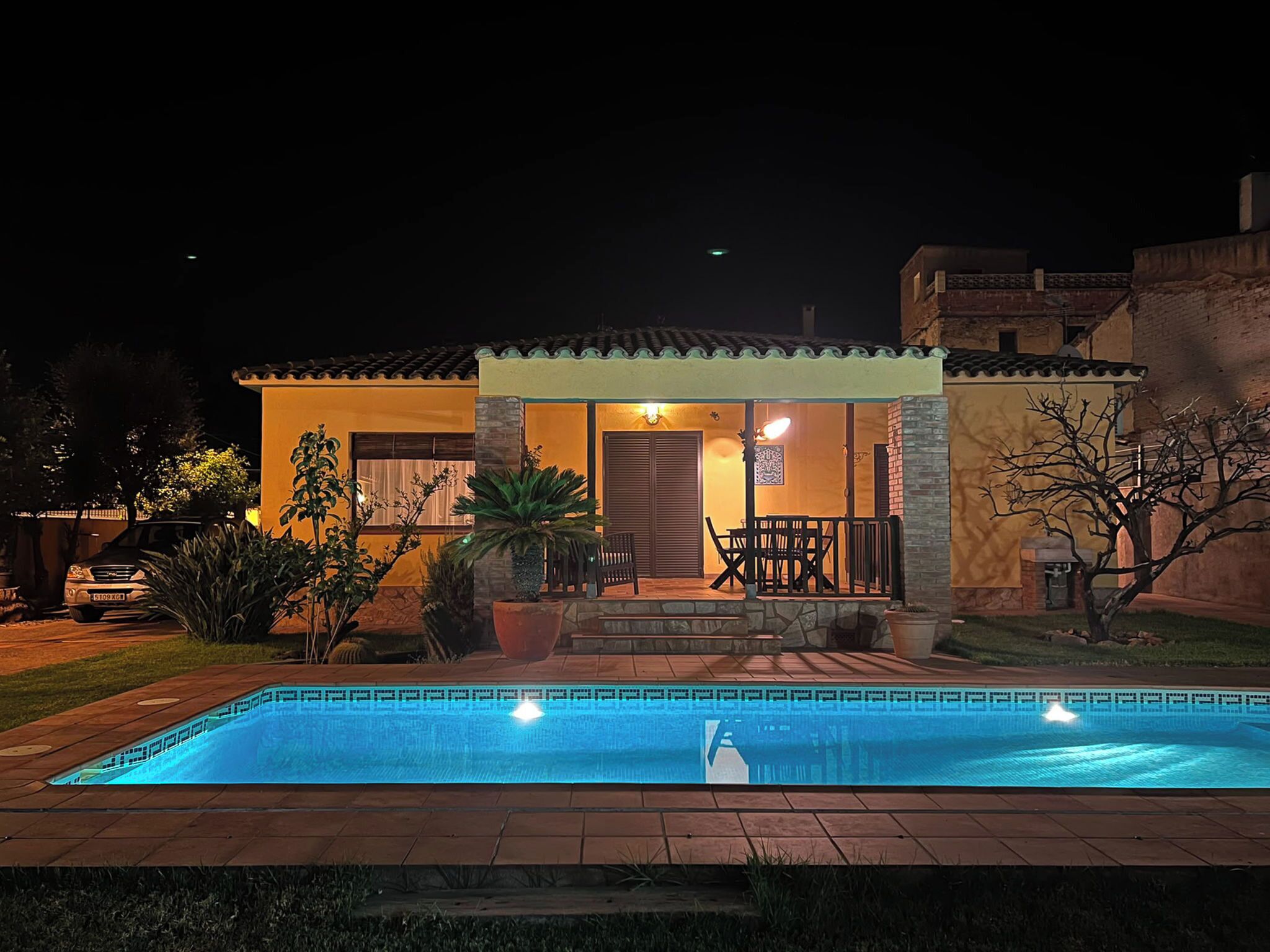 A residential property with a swimming pool, patio furniture, and a well-lit entrance.