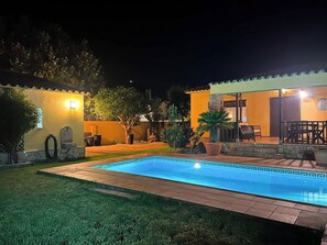 A nighttime view of a residential property with a swimming pool, outdoor furniture, and a well-lit patio area. - Sunrise by Interhome (Vilajuiga)