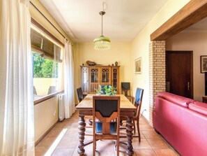 A dining area with a wooden table, chairs, a chandelier, and a red sofa. - Sunrise by Interhome (Vilajuiga)