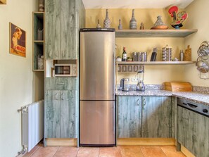 A kitchen with a stainless steel refrigerator, wooden cabinets, a microwave, and various kitchen utensils on shelves. - Sunrise by Interhome (Vilajuiga)