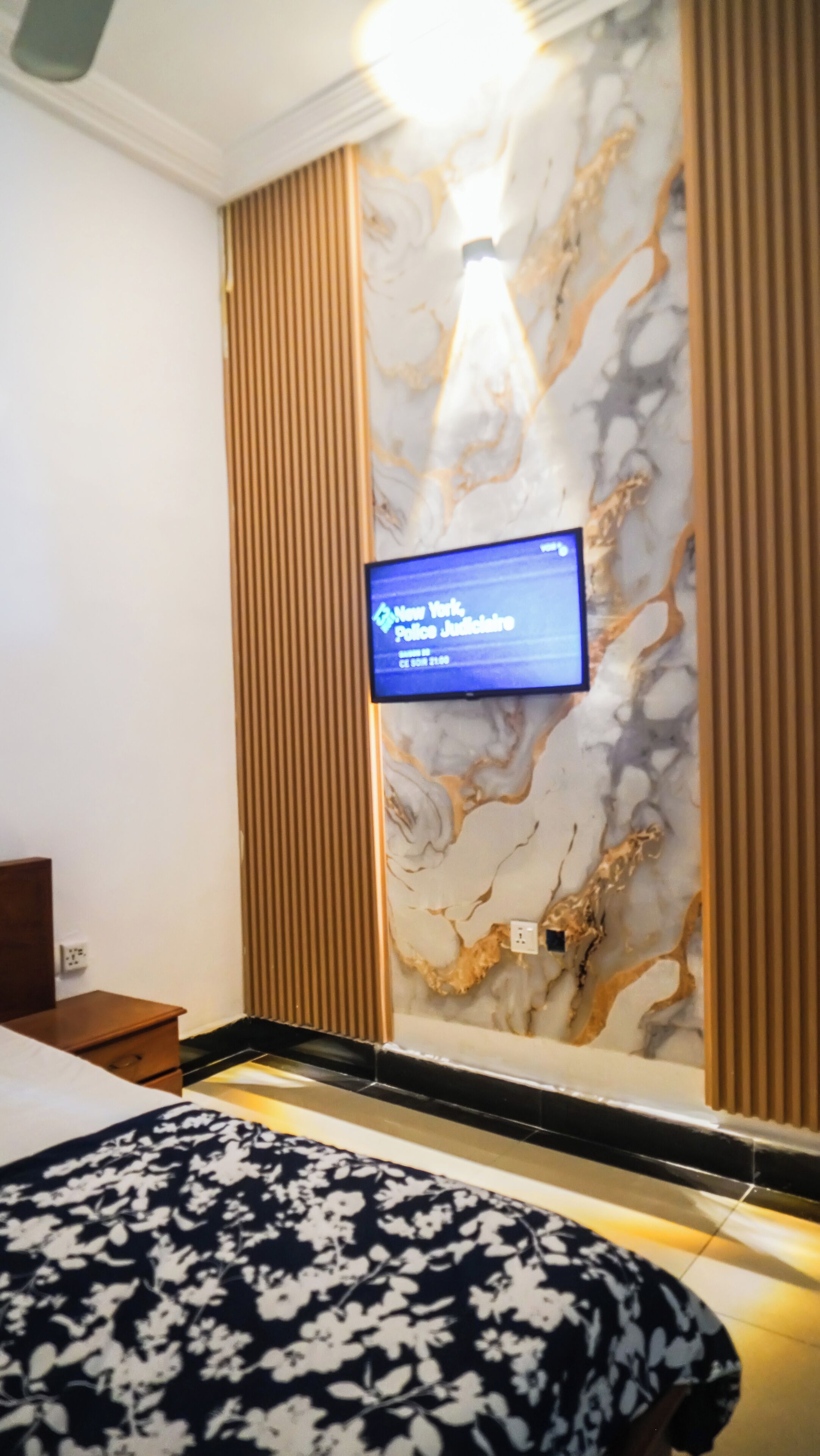 Una habitación de hotel con una cama, un televisor fijado en una pared de mármol y un diseño de paneles de madera.