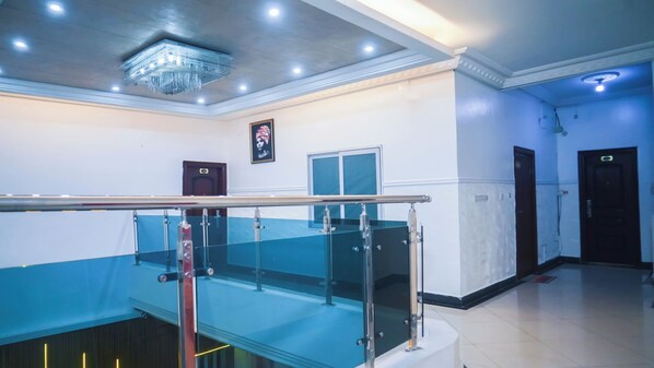 Interior de un hotel con una escalera, una araña y un cuadro en la pared, además de una puerta.