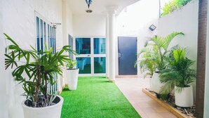 Un pasillo con césped artificial, plantas en macetas y una puerta con paneles de vidrio.