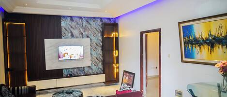 A modern living room with a flat-screen TV, a marble accent wall, a glass coffee table, and a sofa.