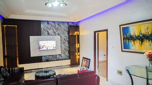 Una sala moderna con televisión de pantalla plana, una pared decorativa de mármol, una mesa de centro de cristal y un sofá.