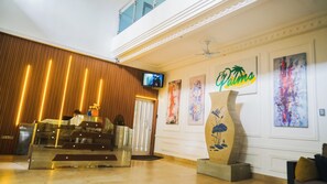 Aula, jossa on puupanelointi yhdellä seinällä, seinälle asennettu televisio ja kyltti, jossa lukee ”The Palms Apartments”.