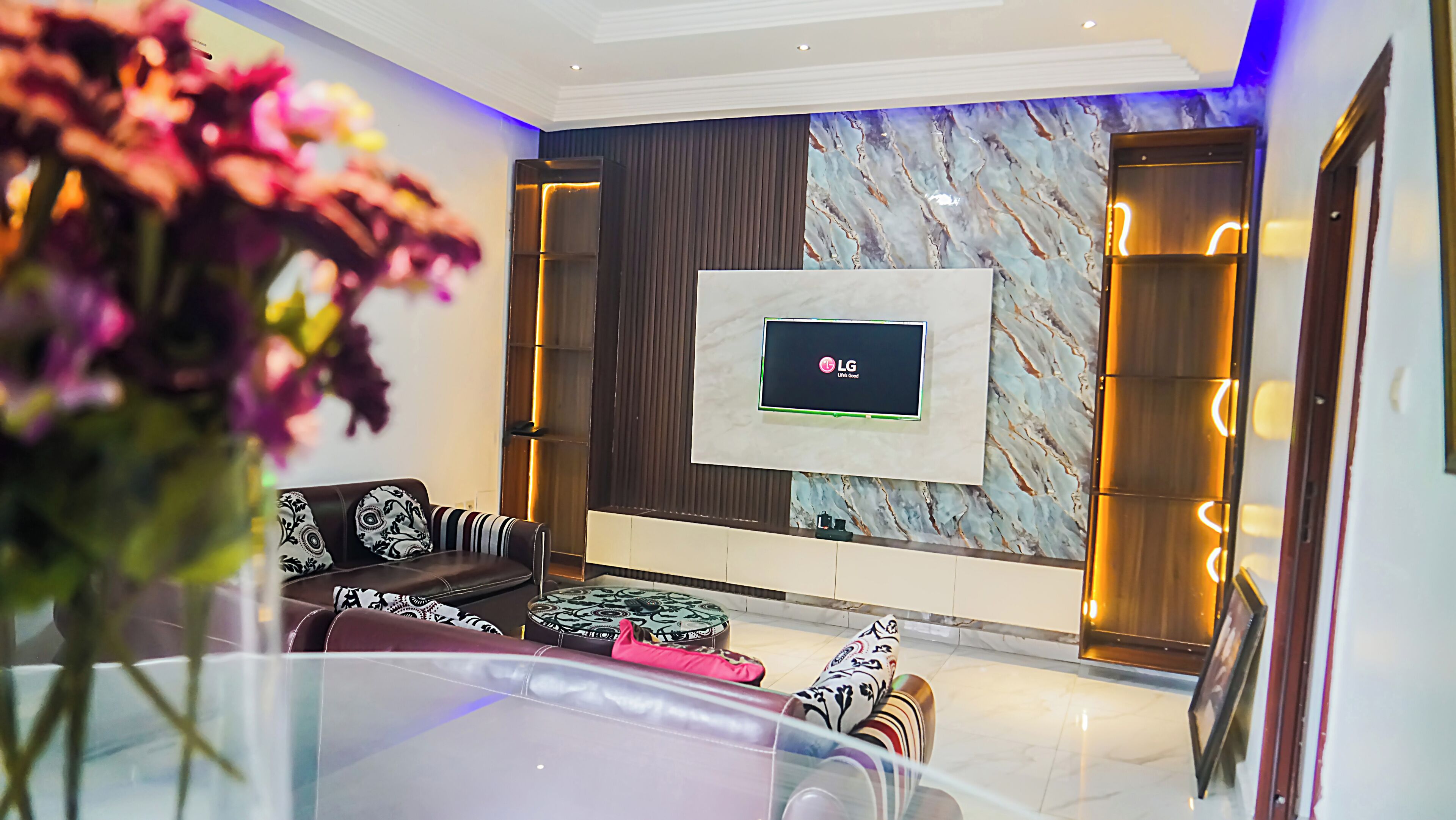 Una sala de estar moderna con un televisor de pantalla plana montado en una pared de mármol, un sofá con cojines estampados y una mesa de centro de vidrio.